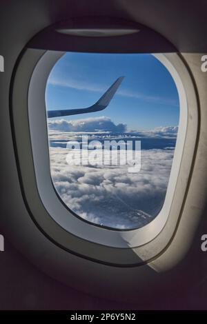 A view from an airplane window showing the wing and clouds in the background Stock Photo