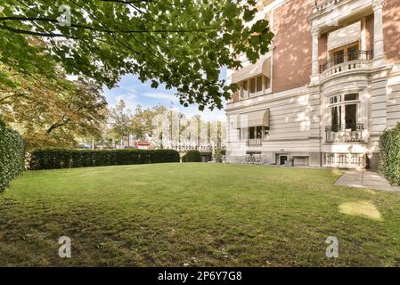 a lawn in front of a large building with a red car parked on the grass and some trees behind it Stock Photo