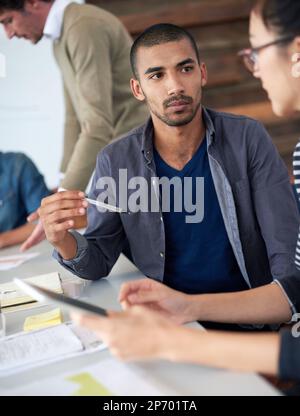 Discussing strategies. two coworkers sitting at a table in an office using a digital tablet. Stock Photo