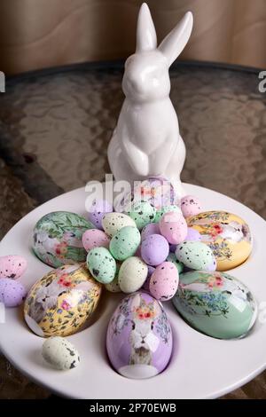 photo of decorative large and small eggs lying on a special plate with a white rabbit standing next to them Stock Photo