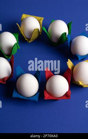 photo a lot of eggs in multi-colored cells stand in a circle on a blue background Stock Photo
