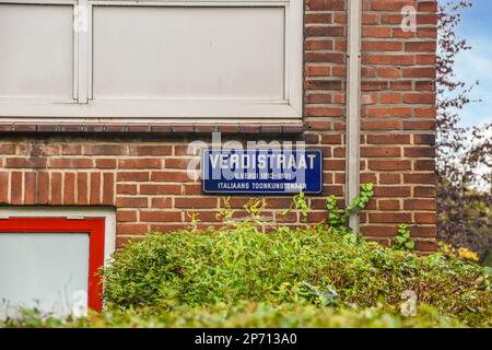 a street sign on the side of a brick building with bushes in front of it and a blue sky background Stock Photo