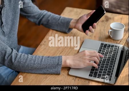 Cropped side view, A male freelancer or businessman remote working at the cafe, using his phone and laptop. Stock Photo
