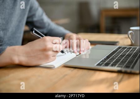 Cropped image of male college student or freelancer noting something on his notepad, remote working at the coffee shop. Stock Photo