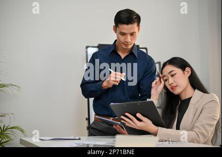 Professional millennial Asian businessman concentrated on working with his female coworker in the office. Stock Photo