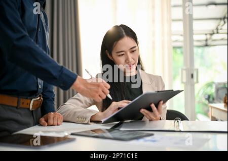 Confused young Asian businesswoman or female office worker being trained by her male boss, working together in the office. Stock Photo
