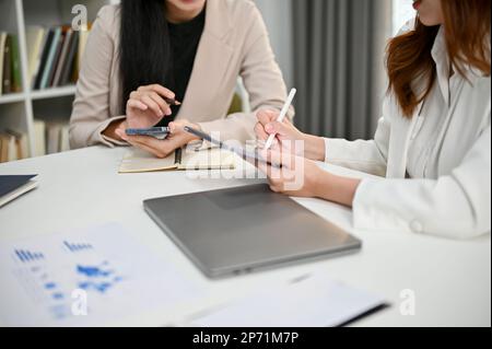 Cropped image of two millennial Asian businesswomen working together, discussing and planing project in the office co-working space. Stock Photo