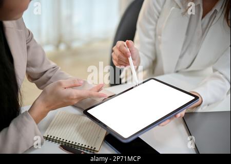 Close-up image of two millennial Asian female office workers discussing work, sharing business ideas, looking at tablet screen. tablet white screen mo Stock Photo
