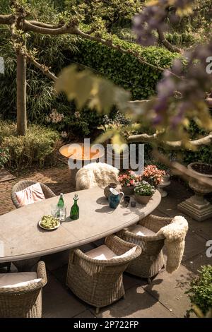 a table and chairs on a patio with flowers in vases, wine bottles and an umbrella over the table Stock Photo