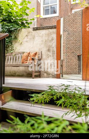 Amsterdam, Netherlands - 10 April, 2021: a bench in front of a building with a cat sleeping on it's back and green leaves surrounding the bench Stock Photo