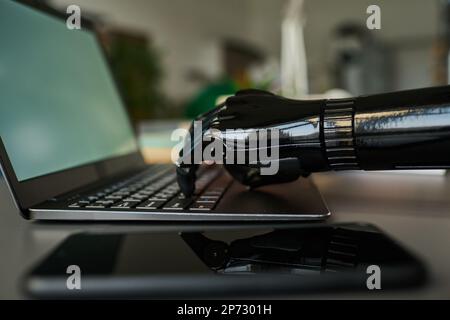 Close-up of business person with prosthetic arm working online typing on laptop at table Stock Photo