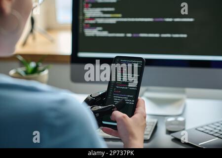 Close-up of IT specialist working with codes on smartphone connecting it with computer and developing software Stock Photo