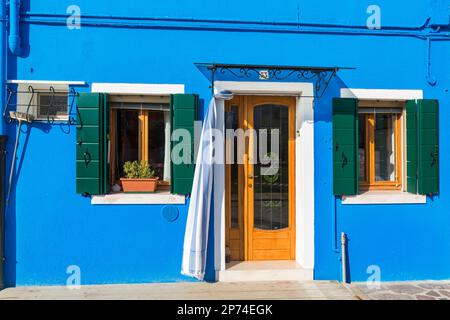 doorway with curtain and windows with shutters on bright bluecoloured house at Burano, Venice, Italy in February Stock Photo