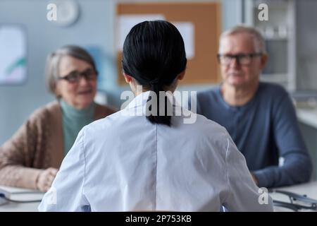 Back view of female doctor working with senior couple in medical clinic, copy space Stock Photo