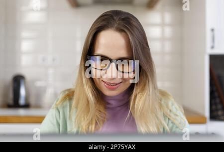 Portrait of happy white woman in glasses reading text from computer screen. Cheerful adult female person working on laptop at home Stock Photo