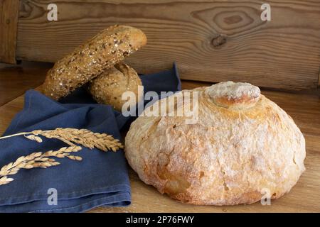 Delicious and freshly baked traditional big round bread close up and two roll bread cereals on the background. Horizontal view. Stock Photo