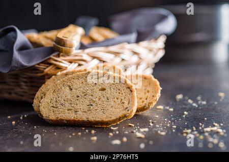 Sliced whole grain bread. Tasty wholegrain pastry with seeds on the black table. Stock Photo