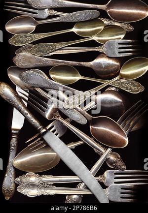 Many antique spoons, knives, forks isolated on black background. Old silver cutlery decorated with floral pattern for serving food. Vintage fancy tabl Stock Photo