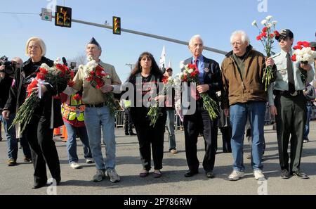 A delegation of protestors and war veterans , including U.S. Army Col. Mary Ann Wright, left, and Daniel Ellsberg , fourth from left, sport coat, carry flowers to place near the Iwo Jima Memorial statue located outside the main gate at Marine Corps Base Quantico , Va, on Sunday afternoon, March 20, 2011. (AP Photo/The Free Lance-Star, Robert A. Martin)