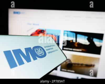 Mobile phone with logo of International Maritime Organization (IMO) on screen in front of website. Focus on center-right of phone display. Stock Photo