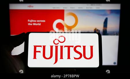 Person holding smartphone with logo of Japanese ICT company Fujitsu Limited on screen in front of website. Focus on phone display. Stock Photo