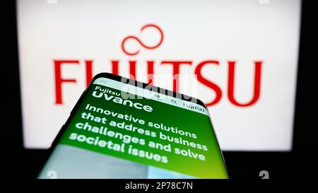 Smartphone with website of Japanese ICT company Fujitsu Limited on screen in front of business logo. Focus on top-left of phone display. Stock Photo