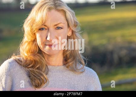 Attractive thoughtful middle aged woman outside smiling in golden hour sunlight Stock Photo