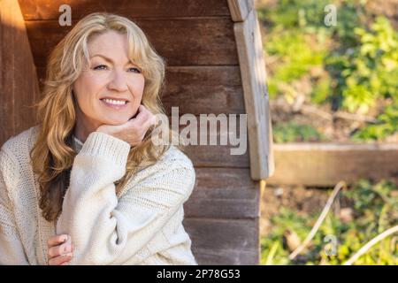 Attractive thoughtful middle aged woman sitting relaxing outside Stock Photo