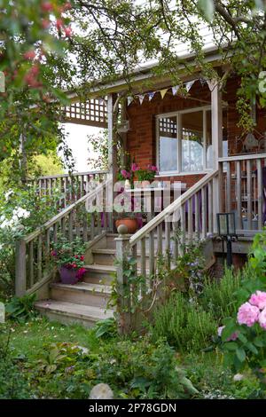 Raised wooden decking area with steps and outdoor seating, surrounded by climbing roses Stock Photo