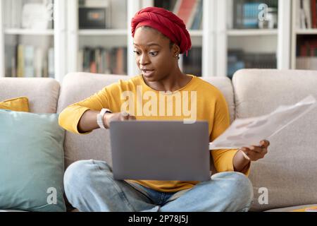Worried young black woman entrepreneur checking watch, working from home Stock Photo