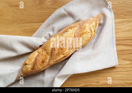 Fresh french baguette on a linen towel, crispy bread, fried crust . Wooden background. Top view, close up. Bakery product. Stock Photo