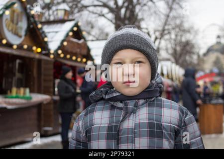The lonely boy stood alone at the Christmas Fair on the street Stock Photo
