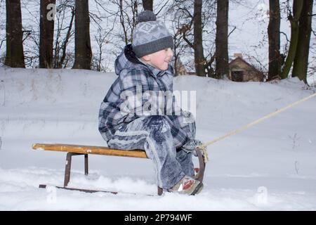 Winter fun - sledding at winter time. Young boy enjoying a sledge ride in a snowy winter park. Stock Photo