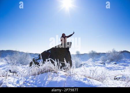 The guy on the rock sits in the winter and makes selfie photos Stock Photo