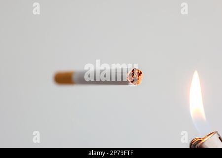 Single unlit cigarette stick close to open flame fire from lighter close up studio shot no people. Stock Photo