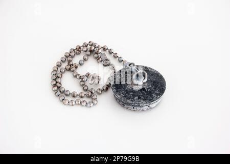 Old dirty limestone scale covered bathtub rubber plug and chain close up shot isolated on white. Stock Photo