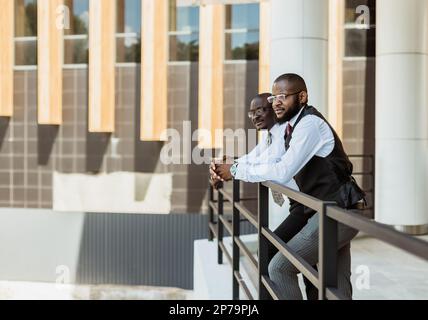 Portrait of two dark-skinned businessmen talking in the background of a modern building exterior. Friendly meeting outdoors Stock Photo