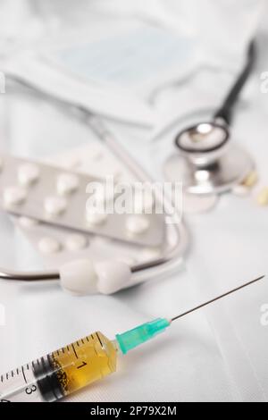 Close-up of a syringe loaded with medication. in the background: pills, stethoscope and doctors gown Stock Photo