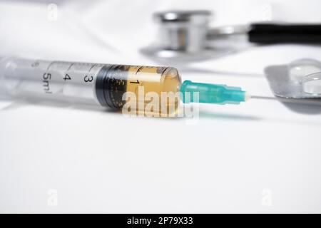 Close-up of a syringe loaded with medication with a stethoscope in the background on a white background Stock Photo