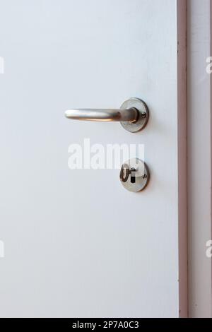 Metal door lock handle and key on wooden white interior door isolated close up shot. Stock Photo