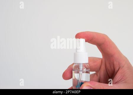 Small plastic hand sanitizer bottle with spray head held in hand by Caucasian male hand isolated close up shot. Stock Photo