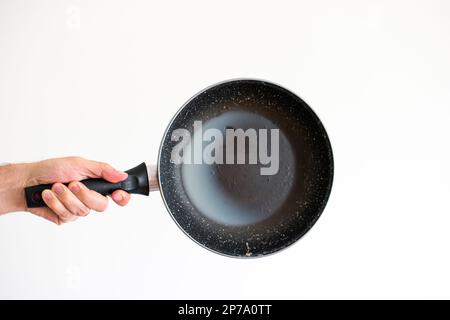 Caucasian male hand holding an old frying pan stained with hardened white lard grease and burned oil isolated on white. Stock Photo