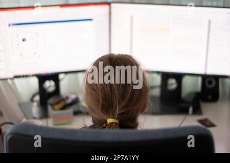 Unrecognizable Caucasian young woman working on the computer from home office with 2 blurry display monitors close up shot shallow depth of field. Stock Photo