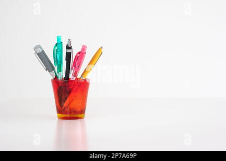 Different colorful pens in a red stained-glass cup isolated on white front view studio shot. Stock Photo