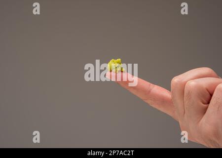 Fresh green Wasabi paste on the pointing fingers of a male hand. Close up studio shot isolated on brown background. Stock Photo