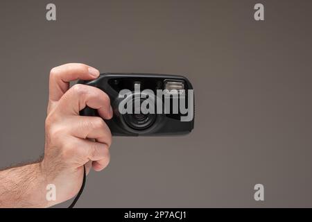 Caucasian male hand holding a generic old film point and shoot camera. Close up studio shot, isolated on brown background. Stock Photo