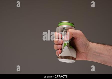 Caucasian male holding a crushed tin metal beer can. Close up studio shot, isolated on brown background. Stock Photo