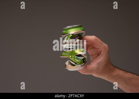 Caucasian male holding two crushed tin metal beer cans. Close up studio shot, isolated on brown background. Stock Photo