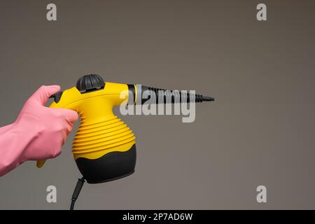 Male hand in rubber glove holding a small steam pressure cleaner. Close up studio shot, isolated on gray background. Stock Photo
