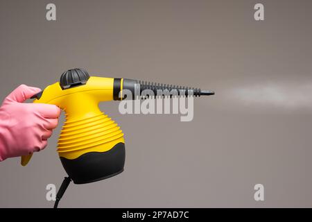 Male hand in rubber glove holding a small steam pressure cleaner. Close up studio shot, isolated on gray background. Stock Photo